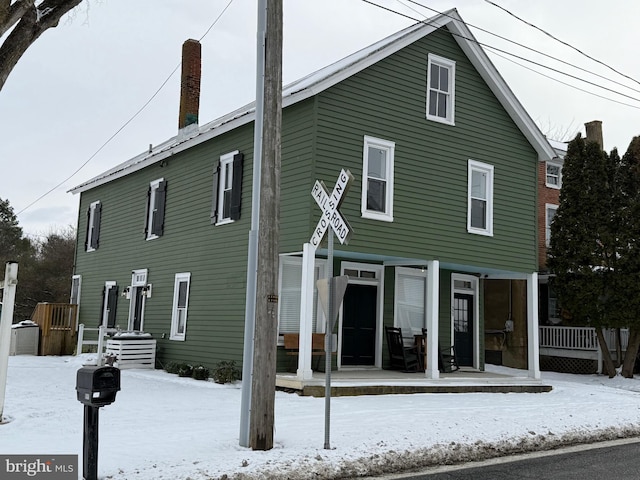 snow covered house featuring covered porch and a chimney