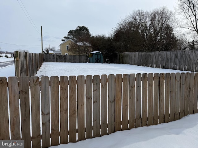 snowy yard featuring a fenced front yard, an outdoor structure, and a storage unit