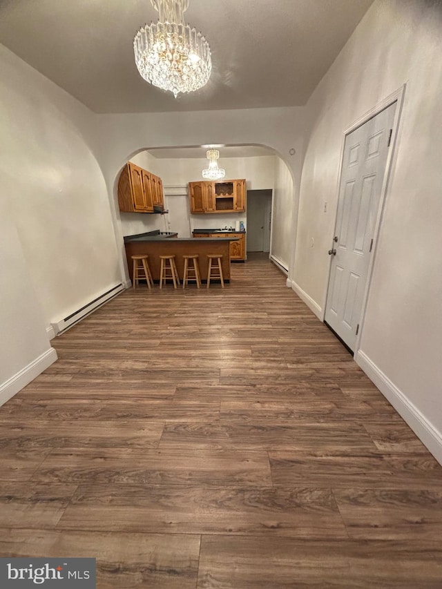 interior space with kitchen peninsula, hanging light fixtures, dark wood-type flooring, a notable chandelier, and baseboard heating