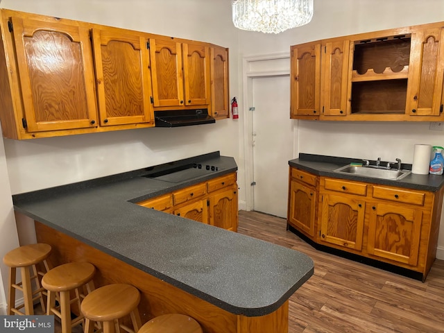 kitchen with kitchen peninsula, dark hardwood / wood-style floors, a notable chandelier, sink, and black cooktop