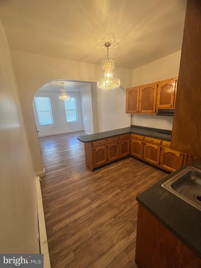 kitchen featuring sink, dark hardwood / wood-style flooring, kitchen peninsula, hanging light fixtures, and a notable chandelier