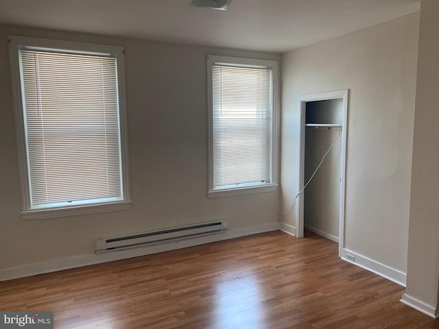 unfurnished bedroom featuring a closet, multiple windows, a baseboard radiator, and hardwood / wood-style floors