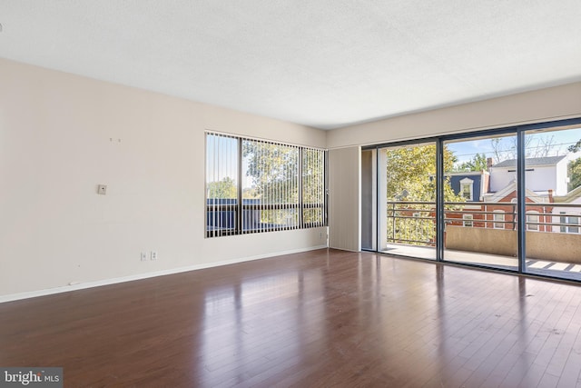 empty room featuring dark wood-type flooring, a textured ceiling, and plenty of natural light