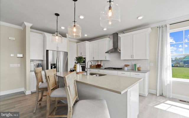 kitchen featuring sink, hanging light fixtures, white cabinetry, stainless steel appliances, and wall chimney exhaust hood