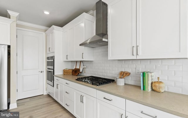 kitchen with wall chimney exhaust hood, white cabinetry, stainless steel appliances, and light wood-type flooring