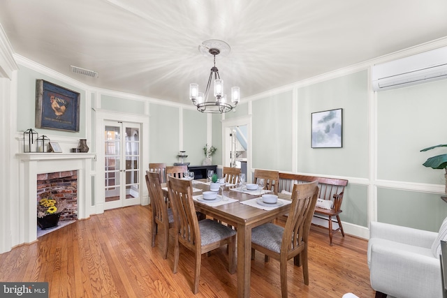 dining room featuring a wall mounted AC, a notable chandelier, wood-type flooring, and crown molding