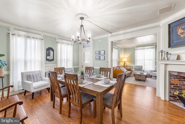 dining area with ornamental molding, a chandelier, a fireplace, and light hardwood / wood-style floors