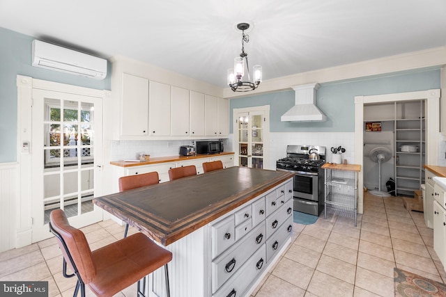 kitchen with a wall unit AC, white cabinets, tasteful backsplash, gas range, and custom range hood