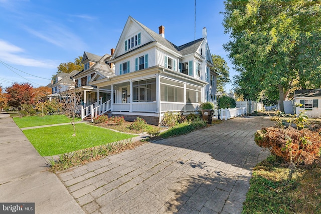 victorian home featuring covered porch, a sunroom, and a front lawn