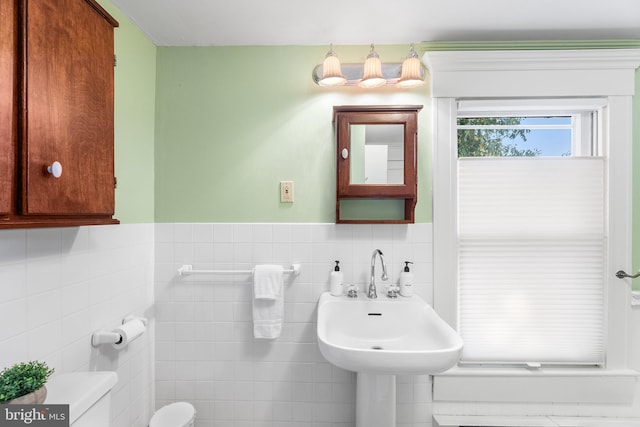 bathroom with toilet, sink, and tile walls