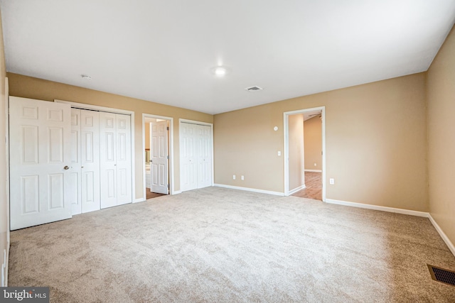 unfurnished bedroom featuring carpet floors and two closets