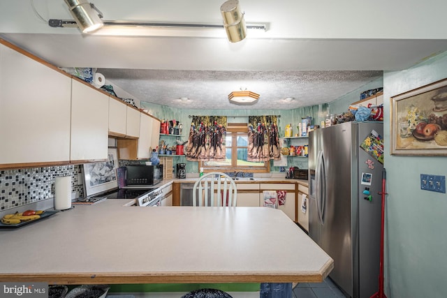 kitchen with tasteful backsplash, a textured ceiling, kitchen peninsula, white cabinetry, and stainless steel appliances