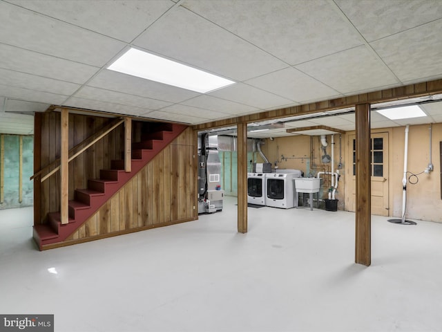 basement with heating unit, washer and dryer, sink, a drop ceiling, and wooden walls