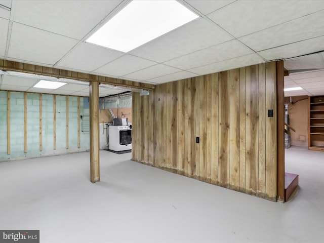 basement featuring a paneled ceiling and wood walls