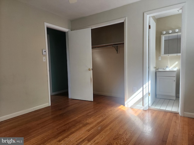 unfurnished bedroom featuring sink, ensuite bathroom, hardwood / wood-style flooring, and a closet