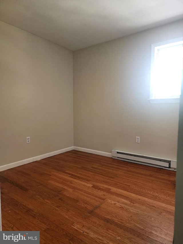 unfurnished room with baseboard heating and dark hardwood / wood-style floors