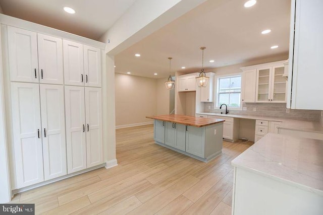 kitchen with white cabinets, hanging light fixtures, wood counters, light hardwood / wood-style flooring, and a center island