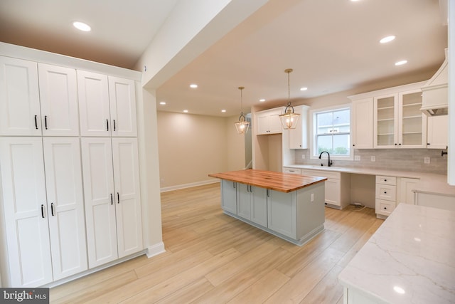 kitchen featuring wood counters, a center island, pendant lighting, white cabinets, and light hardwood / wood-style flooring