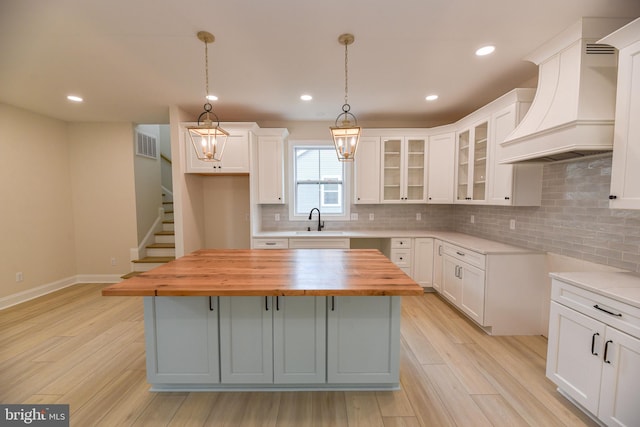 kitchen with a center island, white cabinetry, light hardwood / wood-style floors, wooden counters, and custom range hood