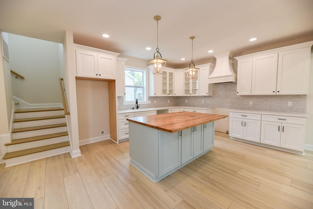 kitchen with custom exhaust hood, white cabinetry, butcher block counters, and a kitchen island