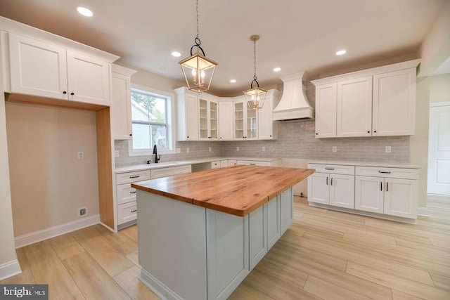 kitchen featuring white cabinetry, wooden counters, custom range hood, and a kitchen island