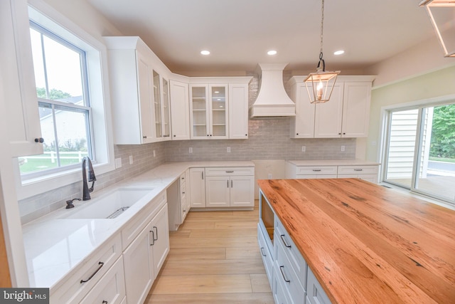 kitchen featuring hanging light fixtures, sink, white cabinetry, custom exhaust hood, and butcher block countertops