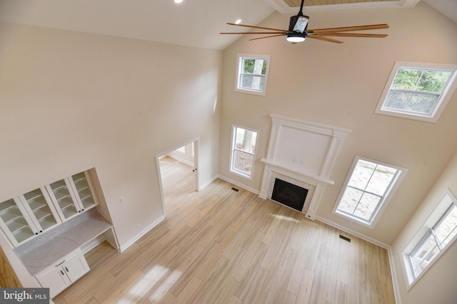 unfurnished living room with light hardwood / wood-style floors, beam ceiling, high vaulted ceiling, and ceiling fan