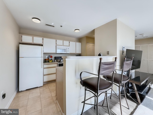 kitchen featuring a kitchen breakfast bar, white cabinetry, light tile patterned floors, and white appliances