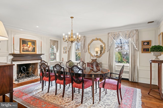 dining room with ornamental molding, a fireplace, hardwood / wood-style floors, and a notable chandelier