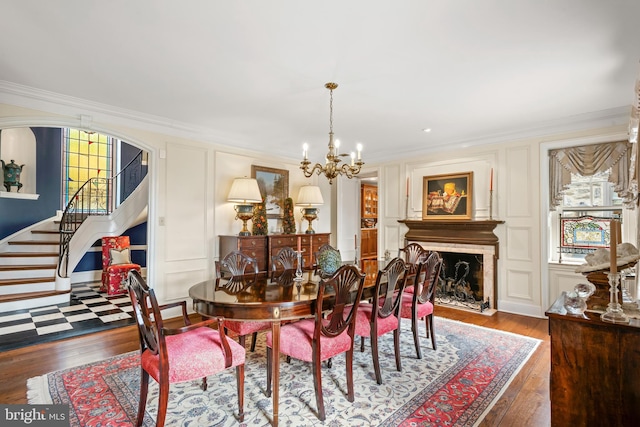 dining area with wood-type flooring, a notable chandelier, crown molding, and a high end fireplace