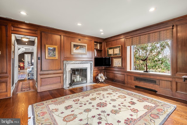 living room featuring a premium fireplace, built in features, and hardwood / wood-style flooring