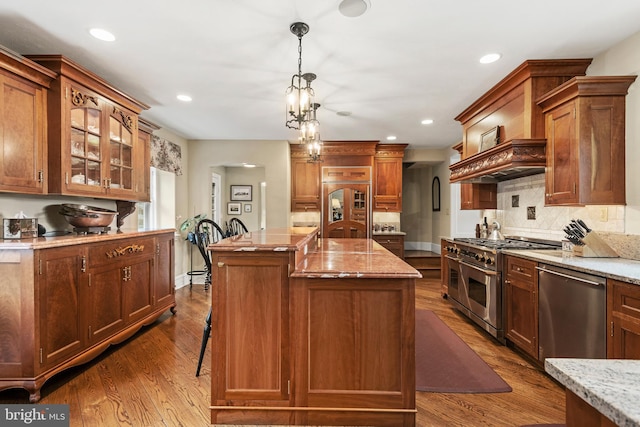 kitchen featuring a kitchen island with sink, high end appliances, pendant lighting, light stone counters, and hardwood / wood-style flooring