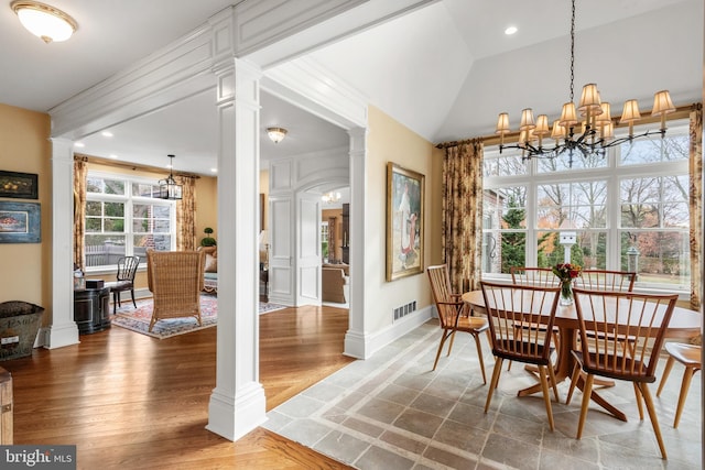 dining space with hardwood / wood-style floors, vaulted ceiling, ornate columns, crown molding, and a notable chandelier