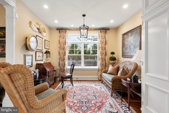 living area featuring decorative columns, light wood-type flooring, and an inviting chandelier