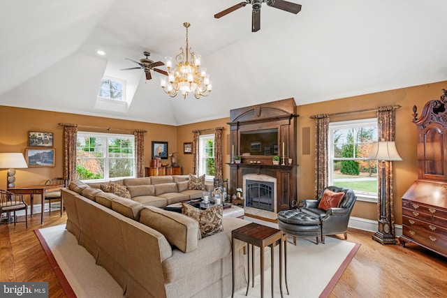 living room featuring light hardwood / wood-style floors, ceiling fan with notable chandelier, lofted ceiling with skylight, and a fireplace