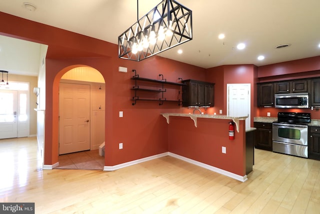 kitchen featuring pendant lighting, light hardwood / wood-style floors, a kitchen bar, dark brown cabinetry, and stainless steel appliances