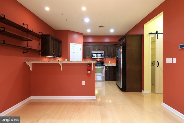 kitchen featuring a barn door, a kitchen bar, light wood-type flooring, and appliances with stainless steel finishes