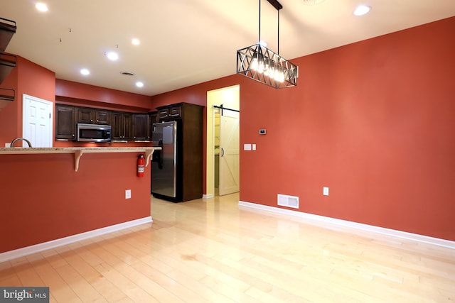 kitchen featuring dark brown cabinets, stainless steel appliances, pendant lighting, a barn door, and a breakfast bar area