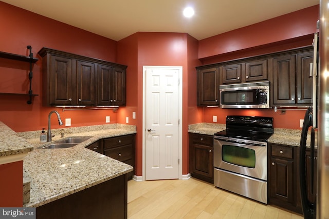 kitchen featuring light stone countertops, light wood-type flooring, stainless steel appliances, and sink