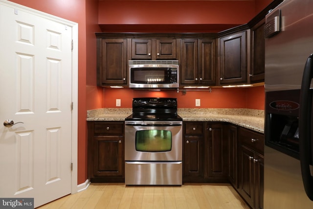 kitchen featuring dark brown cabinets, light wood-type flooring, light stone countertops, and stainless steel appliances