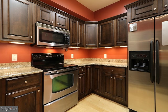 kitchen with dark brown cabinets, light stone counters, appliances with stainless steel finishes, and light hardwood / wood-style flooring