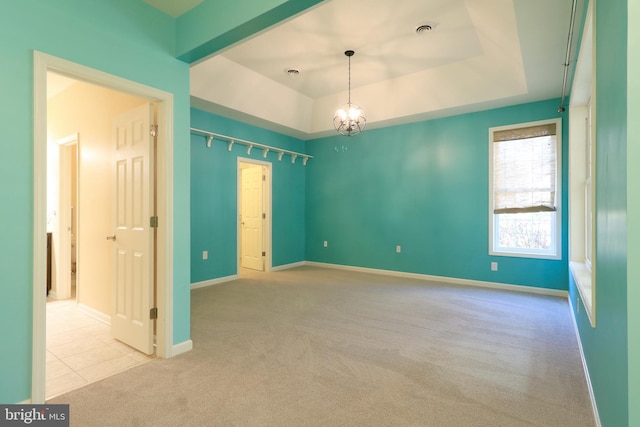 carpeted spare room with a chandelier and a tray ceiling