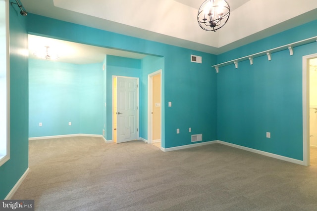 unfurnished room featuring carpet, rail lighting, and an inviting chandelier