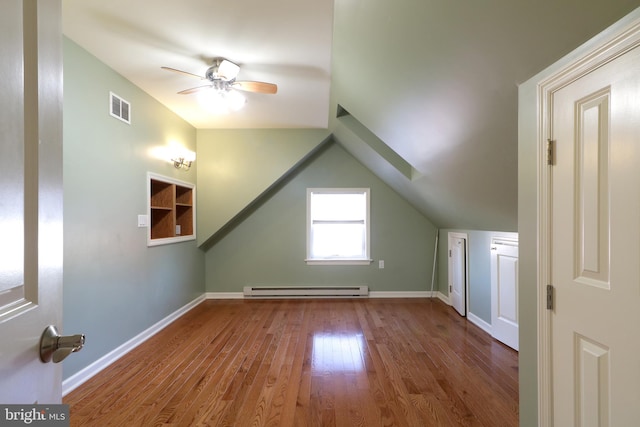 additional living space with ceiling fan, wood-type flooring, lofted ceiling with skylight, and a baseboard heating unit