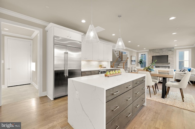 kitchen featuring a center island, decorative light fixtures, stainless steel built in fridge, light stone counters, and white cabinets