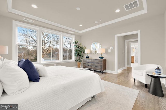 bedroom with a tray ceiling, crown molding, and light hardwood / wood-style flooring