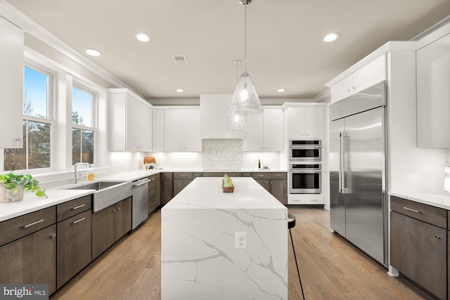 kitchen with appliances with stainless steel finishes, white cabinetry, dark brown cabinets, and decorative light fixtures