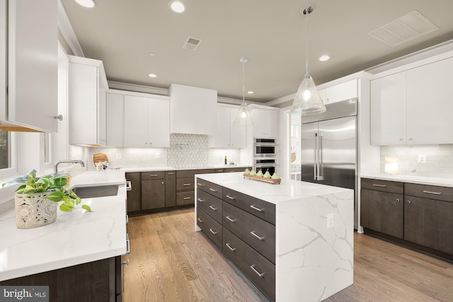 kitchen with sink, a kitchen island, white cabinets, hanging light fixtures, and dark brown cabinetry