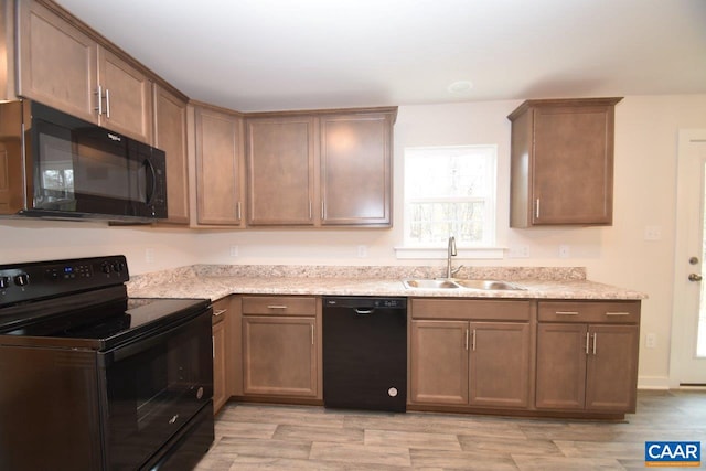 kitchen with light stone countertops, black appliances, sink, and light wood-type flooring