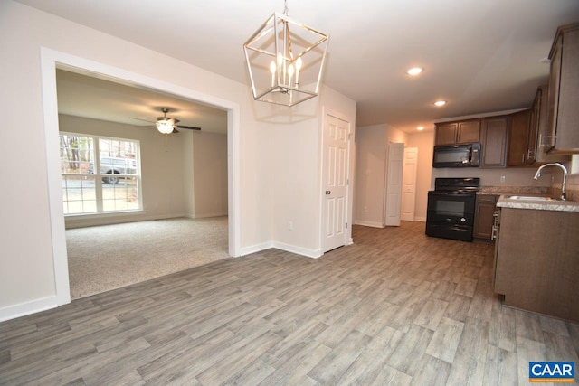 kitchen with wood-type flooring, black appliances, sink, ceiling fan with notable chandelier, and pendant lighting